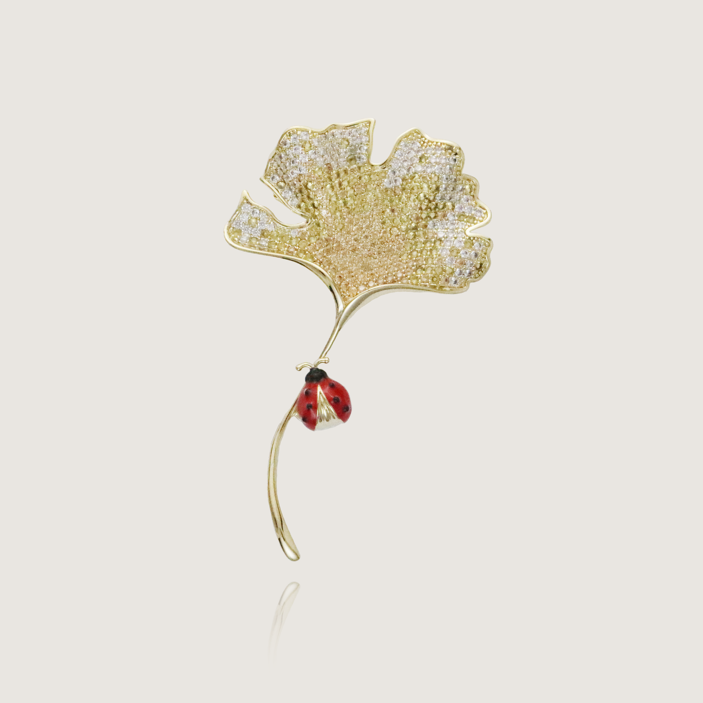 Nature-inspired ginkgo brooch with a sparkling surface and a red ladybug accent.